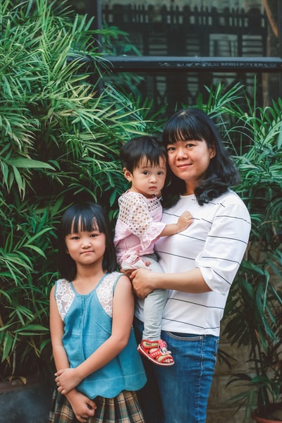 穿蓝色无袖衬衫的女人抱着穿白色和粉色花裙子的女孩